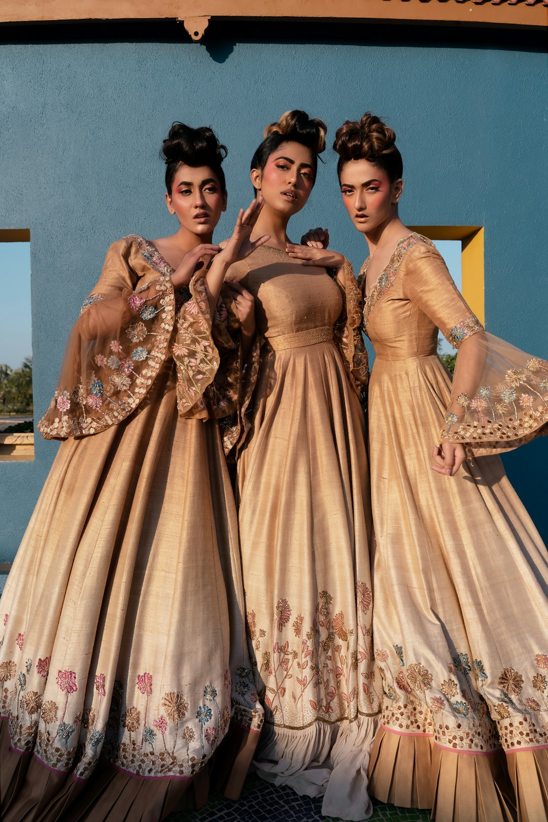 three-women-in-ornate-gowns-against-blue-wall-x-rctolrc8c